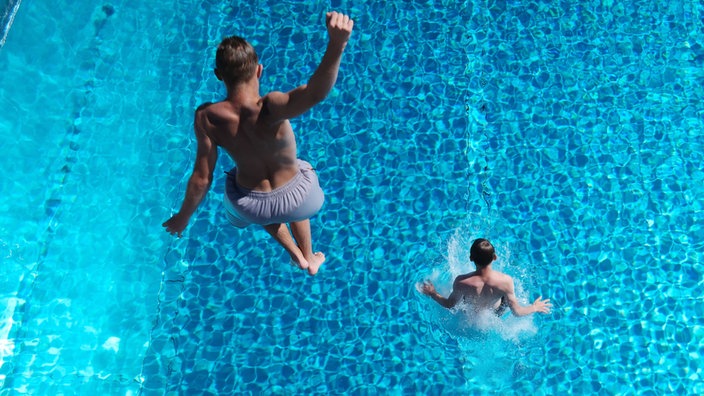 Personen springen von einem Sprungturm ins Wasser.