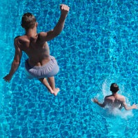 Personen springen von einem Sprungturm ins Wasser.