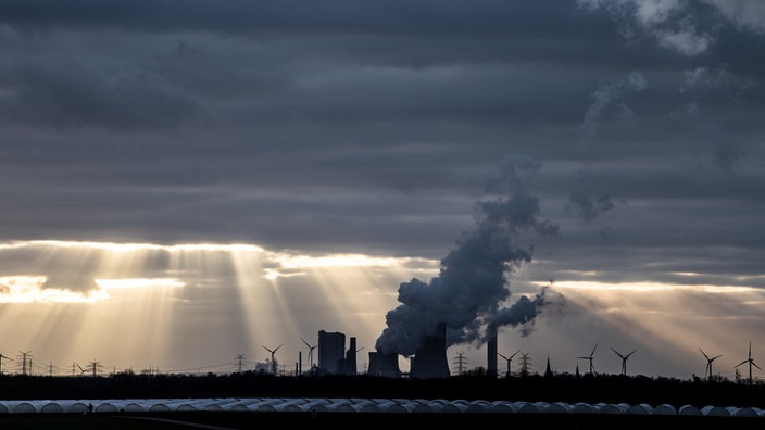 Die Sonne bricht durch eine dicht Wolkendecke über dem Kohlekraftwerk Niederaußem