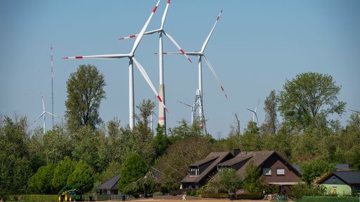 Hinter einer Wohnsiedlung ragen Windräder empor