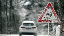 Ein Auto fährt bei winterlichen Verhältnissen über eine Landstraße mit Warnschild