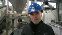 Mann mit blauem Helm steht vor einer Maschine 