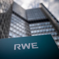 Schild mit der Aufschrift "RWE" vor einem modernen Hochhaus mit Glasfassade im Hintergrund.