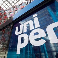Großes blaues Schild mit weißer Aufschrift „uni per“ vor einer modernen Glas- und Stahlkonstruktion eines Gebäudes.