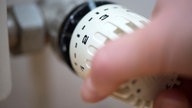 Eine Hand bedient den Thermostatregler an einem Heizkörper 