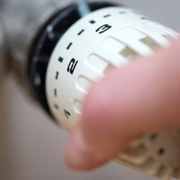 Eine Hand bedient den Thermostatregler an einem Heizkörper 