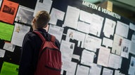 Ein junger Mann steht vor einer Pinnwand mit Wohnungssuchanzeigen- und Angeboten