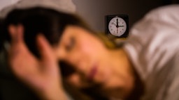 Eine Frau schläft neben einem Wecker, welcher auf 3 Uhr zeigt.