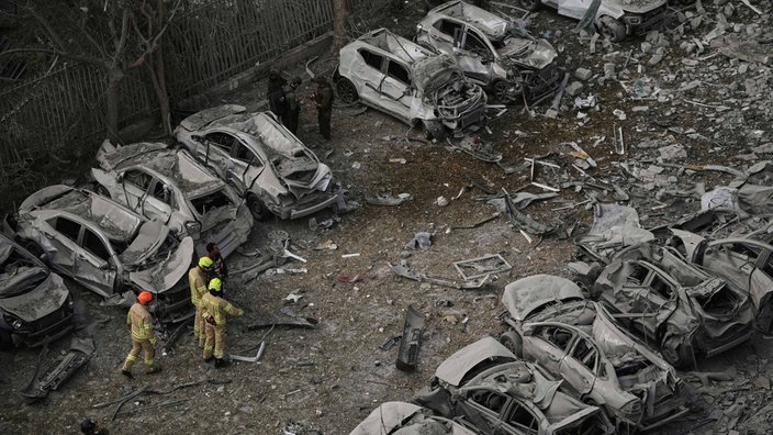 Zerstörte Autos in Israel nach iranischen Angriffen am Dienstagmorgen - dazwischen drei Feuerwehrleute.