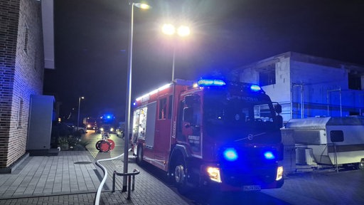 Im Dunklen steht ein Feuerwehrwagen neben einem backsteinen Haus. Ein Schlauch liegt auf dem Boden