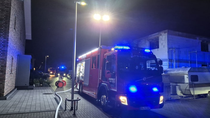 Im Dunklen steht ein Feuerwehrwagen neben einem backsteinen Haus. Ein Schlauch liegt auf dem Boden