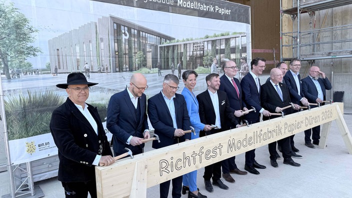 Mehrere Personen stehen mit einem Hammer in der Hand vor einem Holzbalken. 