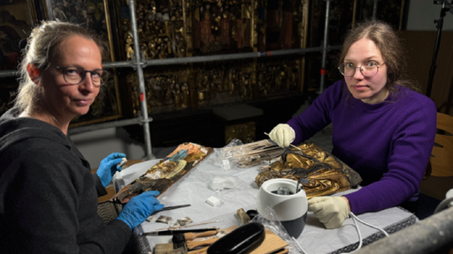zwei Restauratorinnen reinigen Holzfiguren mit Schwämmchen