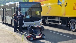 Polizeibeamte stehen vor Bus und untersuchen Unfall mit Rollstuhlfahrer.