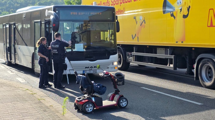 Polizeibeamte stehen vor Bus und untersuchen Unfall mit Rollstuhlfahrer.