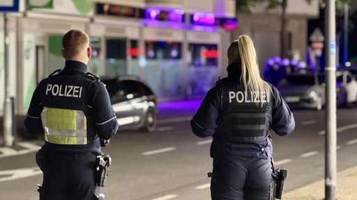 Zwei Polizisten stehen nachts in der Euskirchener Innenstadt mit dem Rücken zur Kamera auf einer Straße. Im Hintergrund ist eine Shisha-Bar zu erkennen.
