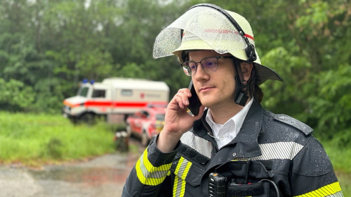  Feuerwehrmann Christian Heinrichs von der Feuerwehr Euskirchen steht draußen im Regen und telefoniert.