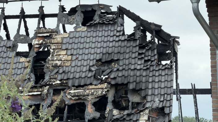 Das Bild zeigt das Dach des abgebrannten Hauses, das teilweise eingebrochen und löchrig ist.