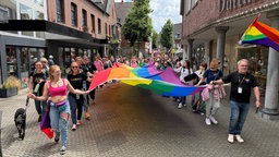 Menschen laufen mit einer riesigen tuchartigen CSD Flagge durch eine Straße.