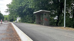 Eine hohe weiße Bordsteinkante an einem breiten Gehweg vor einer Haltestelle