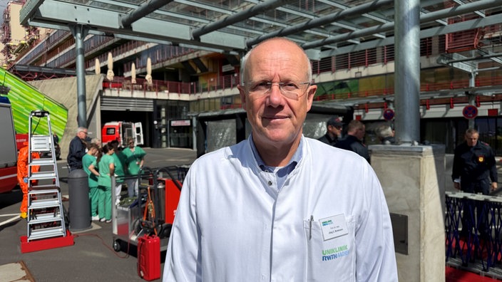 Portrait von Prof. Dr. Jörg Brokmann vor der Aachener Uniklinik, hinter ihm einige Mitarbeitende