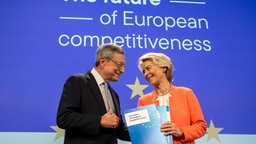 Mario Draghi übergibt einen Report auf der Bühne an Ursula von der Leyen