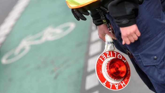 Ein Polizist hält eine Polizeikelle, im Hintergrund erkennt man einen Radweg