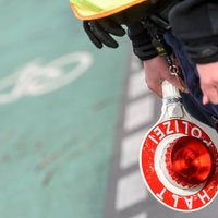 Ein Polizist hält eine Polizeikelle, im Hintergrund erkennt man einen Radweg