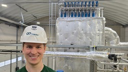 Ein lächelnder junger Mann mit Helm vor einer großen Anlage