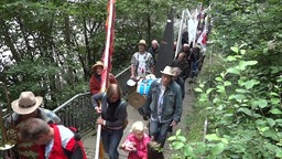 Frauen und Männer ziehen im Protestmarsch mit Fahnen und Segel an einem Bach entlang