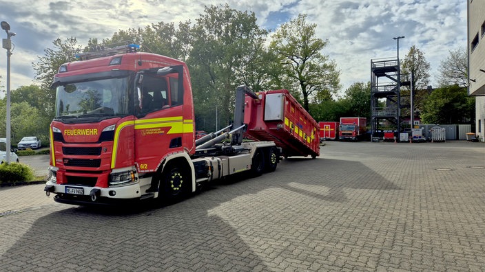 Ein roter Lkw der Feuerwehr beim Aufladen eines Containers