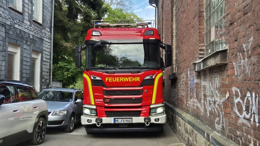 Ein Feuerwehrauto quetscht sich zwischen Mauer und parkenden Autos durch