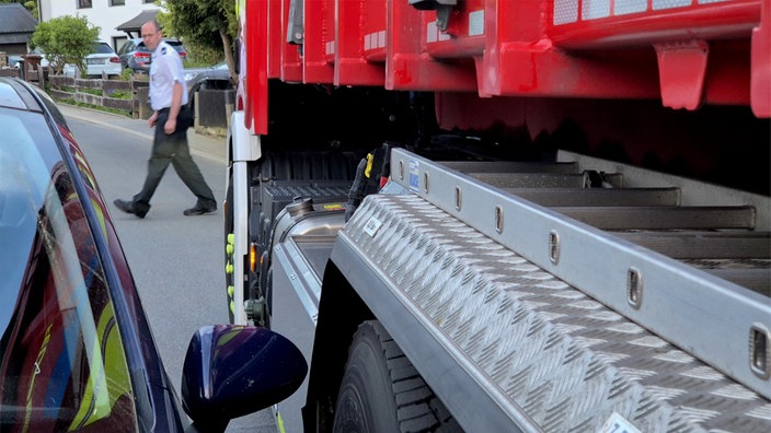 Feuerwehrauto quetscht sich an parkendem Auto vorbei, Mann schaut zu