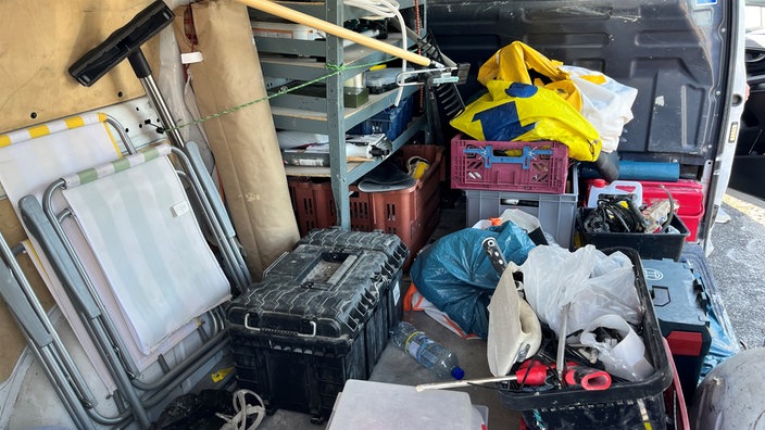 Diverse Boxen aus Plastik, Planen und Liegen auf der Ladefläche eines Transporters