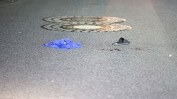 Mitten auf der Straße liegen ein blaues Tuch, ein Schuh und ein Blutfleck ist zu sehen
