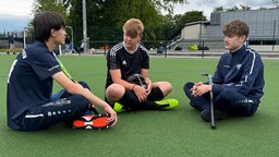 Drei der Jungs aus der Mannschaft sitzen zusammen auf dem Hockeyrasen