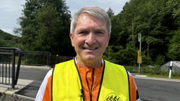 Ein Mann in einer Warnweste schaut lächelnd nach vorne.