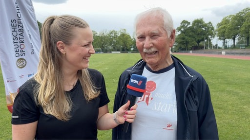 Moderatorin interviewt Mann in Trainingsanzug