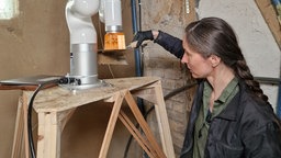 Aleksandra Konopek schmiert Lehm auf eine Kelle, die an einem Roboterarm hängt.