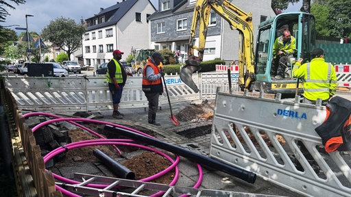 Eine Baustelle mit mehreren Bauarbeitern und einem Minibagger.