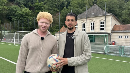 Denzel und Fabian stehen mit einem Fußball auf dem Fußballplatz