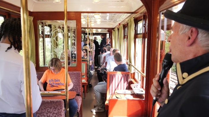 Ein Mann spricht im Kaiserwagen in ein Mikrofon und die Fahrgäste schauen aus dem Fenster