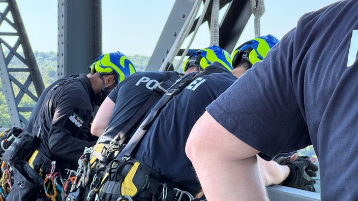Männer in blauen Tshirts mit der Aufschrift "Polizei" und in Sicherheitshelmen schauen über eine Brüstung