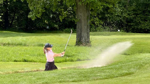 Eine Golferin schlägt Ball aus Bunker
