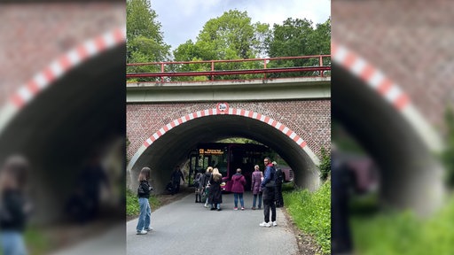 Mehrere Personen stehen vor einer Bahnunterführung, unter der ein Bus stecken geblieben ist.