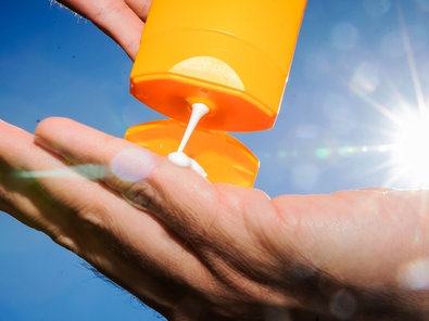 Sonnenmilch aus einer Tube auf eine Hand, im Hintergrund scheint die Sonne von rechts.