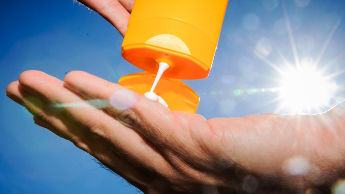 Sonnenmilch aus einer Tube auf eine Hand, im Hintergrund scheint die Sonne von rechts.