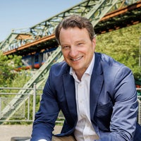 Dr. Hagen W. Lippe-Weißenfeld sitzt vor der Schwebebahnbrücke