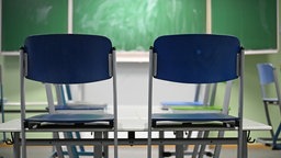 Zzwei auf den Tisch hochgestellte blaue Stühle vor einer grünen Tafel