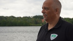Michael Silió-Funk Vorsitzender des "Paderborner Angelvereins" steht am Ufer des Lippesees und blickt vom rechten Bildrand aus über den See.